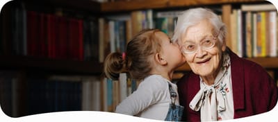 An elderly woman smiling with a young girl in a library setting.
