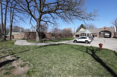 Exterior view of Manoogian Manor with trees and parking