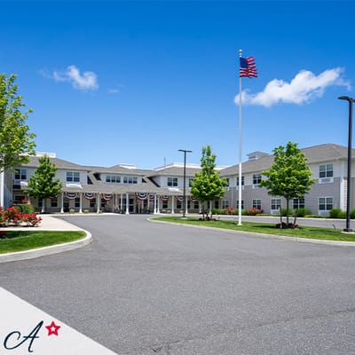 Exterior view of an assisted living facility with trees and flag