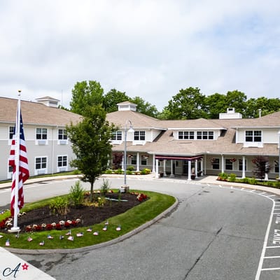 Front view of All American Assisted Living at Raynham with flag and landscaping