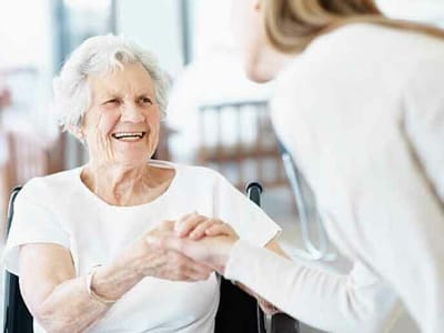 Smiling resident in a wheelchair holding hands with caregiver