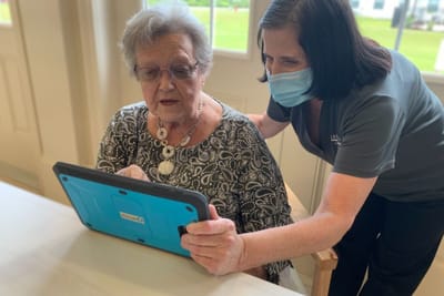 Staff assisting a resident with a tablet in a communal area