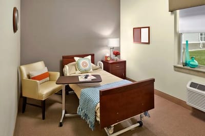 A well-furnished private resident room with a bed and chair