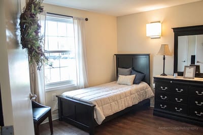 Brightly lit private resident room with bed and dresser