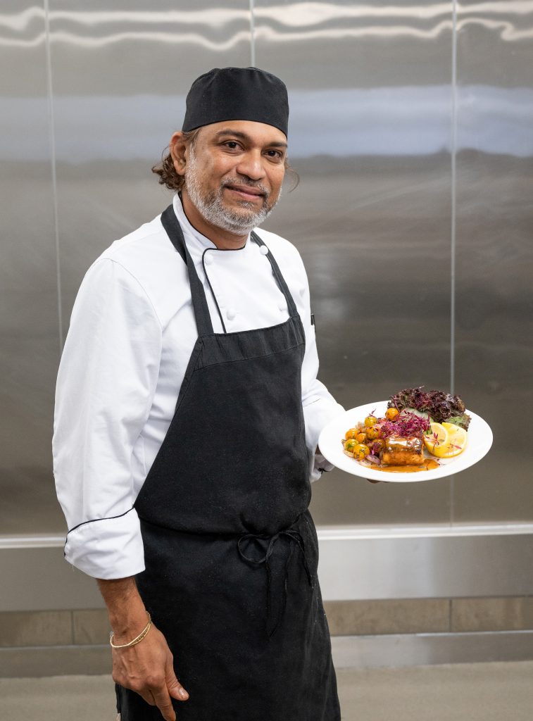 A chef holding a beautifully plated dish in the kitchen