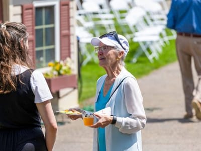A senior woman enjoying a snack outdoors with a staff member