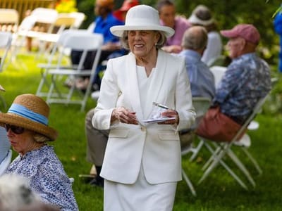 A resident in a white suit at an outdoor event with guests.