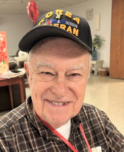 An elderly veteran smiling indoors with a cap
