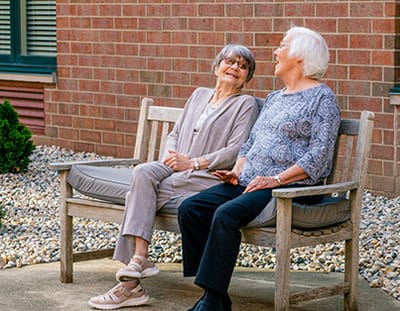 Two residents laughing on a bench outdoors