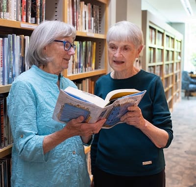 Two residents reading a book together in a library space