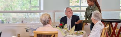Residents enjoying a meal in the dining room with staff interaction