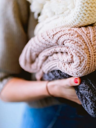 A person holding a stack of knitted blankets