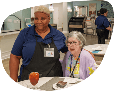 Staff member with a resident enjoying dessert in a dining area
