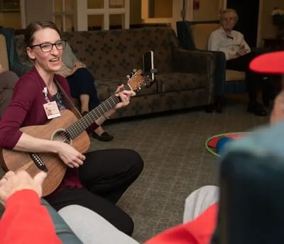 Staff member playing guitar for residents in a common area