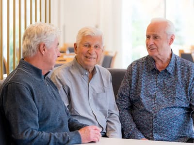 Three elderly men chatting in a common area.