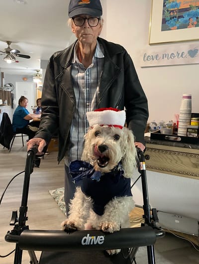 Senior with a walker and a dressed-up dog in a common area.