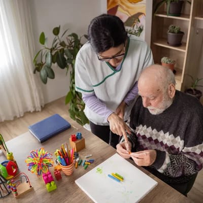 Caregiver assisting senior with art activity.