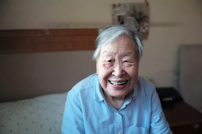 An elderly woman smiling warmly in her room