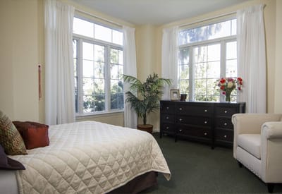 A cozy resident room with a bed and windows.
