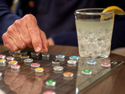 A hand playing a board game with a drink nearby