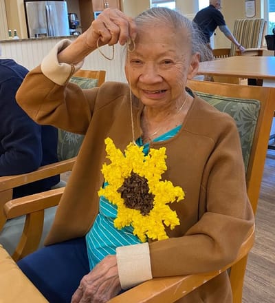 Resident displaying a crafted sunflower in an activity room