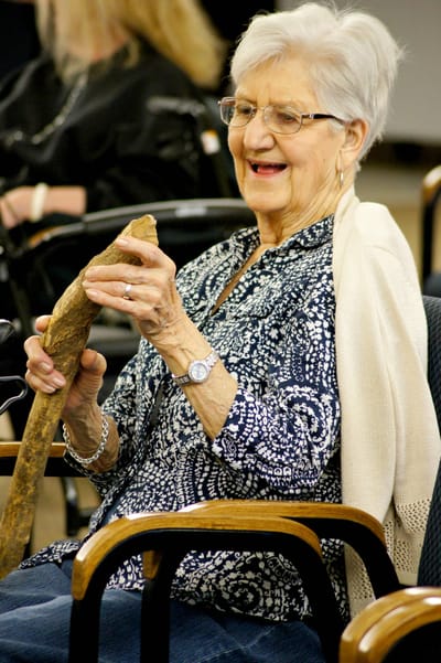 An elderly woman laughing while holding a stick
