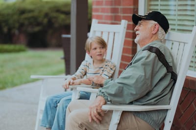 An elderly man talking with a young boy on a porch