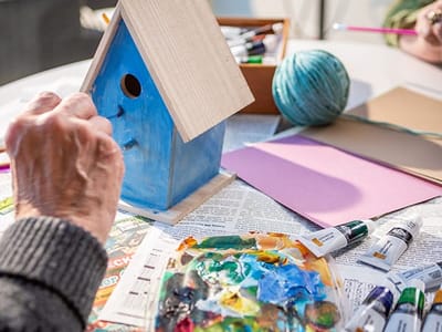 An elderly person painting a birdhouse during an art activity
