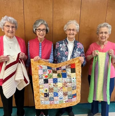 Four residents proudly displaying their handmade quilts