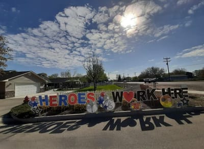 Sign displaying 'Heroes Work Here' in a landscaped area.
