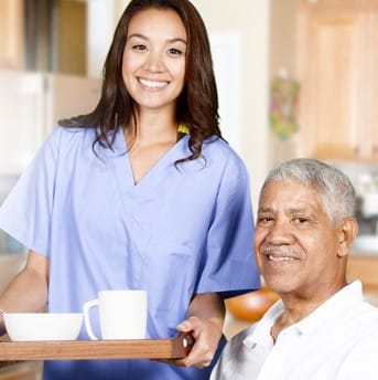 A smiling caregiver serves food to an elderly man.