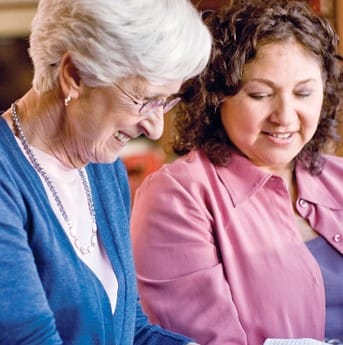 Two women smiling while looking at a notebook together
