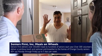 Senior man greeting Meals on Wheels volunteer at door.