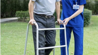 A nurse assisting a senior with a walker in a garden