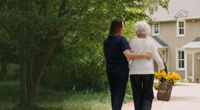 A caregiver assisting a resident outdoors near the facility