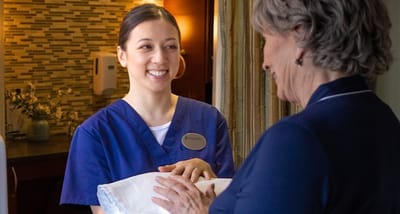 A caregiver smiling while handing a blanket to a resident.