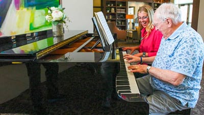 Residents and staff playing piano together in a common area