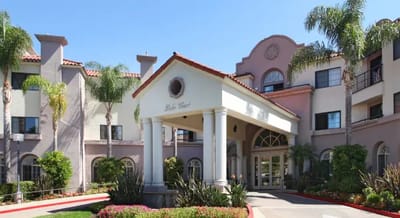 Entrance of a senior living facility with palm trees and flowers