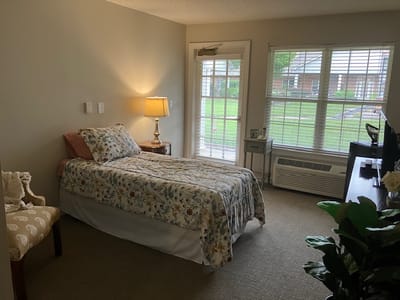 A cozy bedroom with a bed, lamp, and window overlooking a garden.