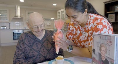 Staff member frosting a cupcake with a resident.