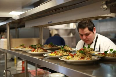 In the kitchen, staff plating meals with colorful garnishes