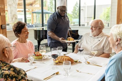 Residents enjoying a meal at a dining table with staff serving food