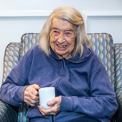 Resident smiling while holding a coffee mug in a cozy chair