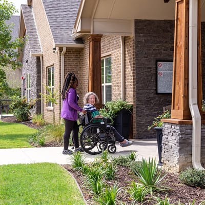 A staff member assisting a resident in a wheelchair outside the facility