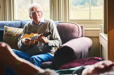 Senior man playing the ukulele in a cozy indoor setting