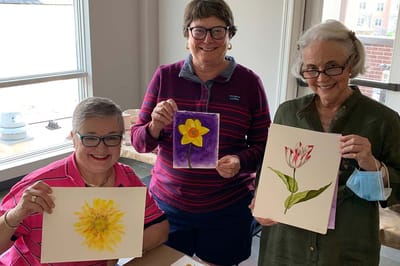 Residents holding their watercolor paintings in an activity room