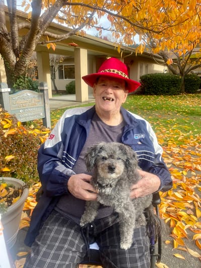 Resident in a red hat with a small dog outdoors
