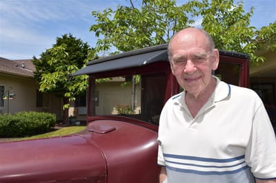A resident standing next to a vintage car in an outdoor space