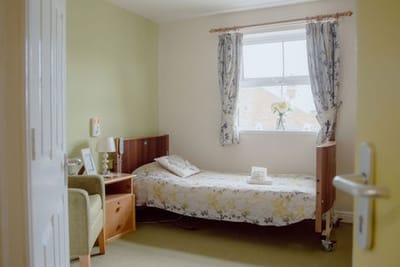 Cozy resident room with floral bedding and window.
