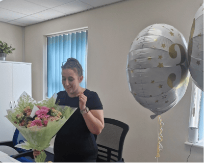 Staff member celebrating with flowers and balloons.